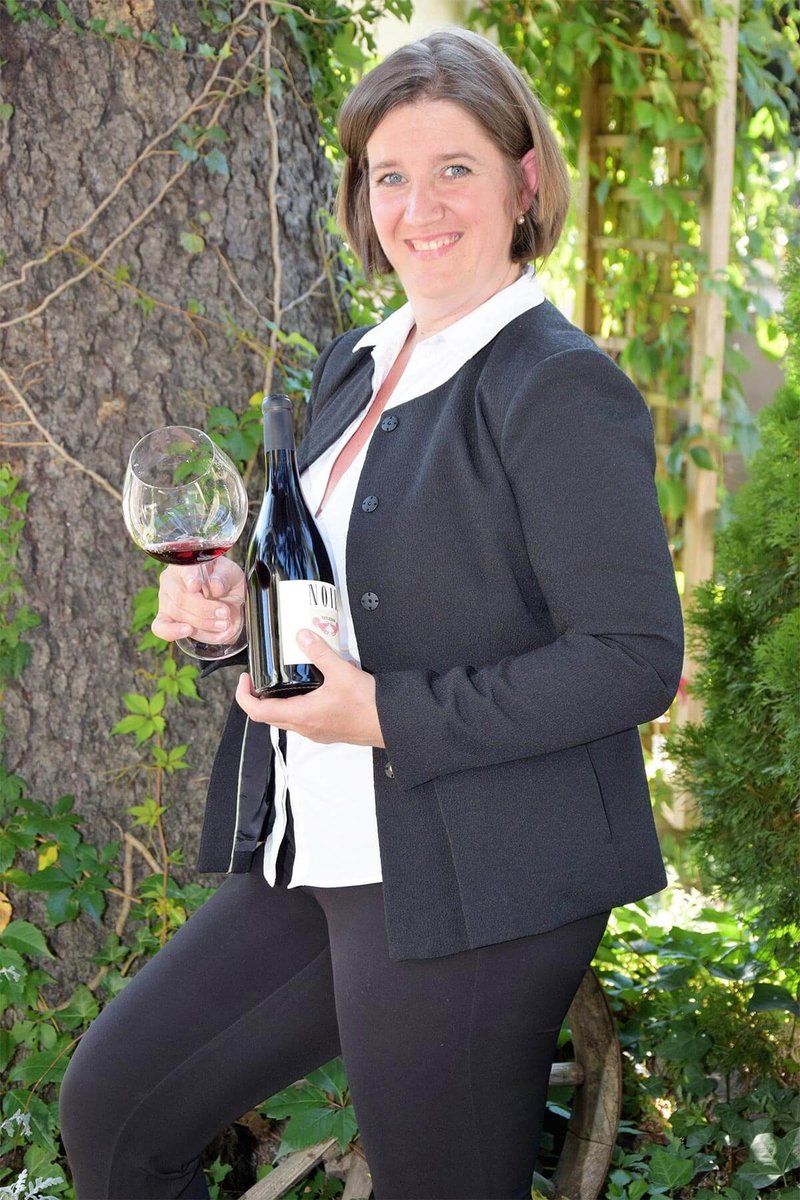 Doris Siller im Garten mit einem Glas Rotwein und einer Weinflasche